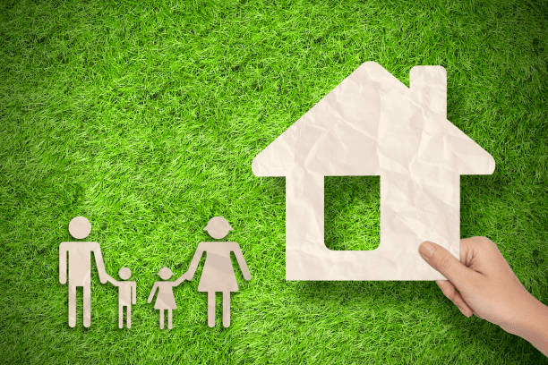 Famille et petit enfant à gauche, main tenant une maison en papier sur gazon vert, symbolisant un déménagement longue distance bouche du rhône
